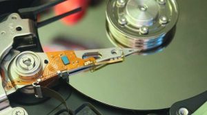 Wnętrze dysku twardego z elementami metalowymi i zielonkawą obudową, widoczne głowice i mechanizmy w procesie niszczenia danych w Poznaniu.