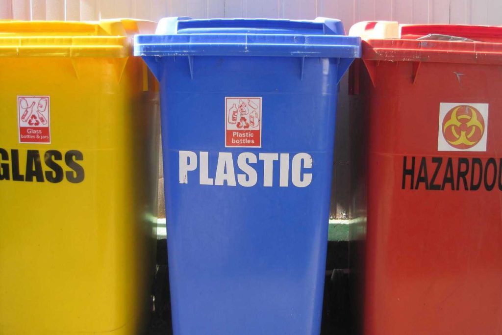 Niebieski pojemnik na odpady z napisem PLASTIC BOTTLES, obok żółty i czerwony kosz do segregacji: ZSEE i grupy odpadów.