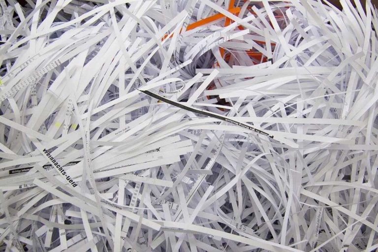 Gęsto ułożone białe pocięte pasy papieru i ścinki wypełniają pojemnik, wśród nich widoczne fragmenty drukowanego tekstu.